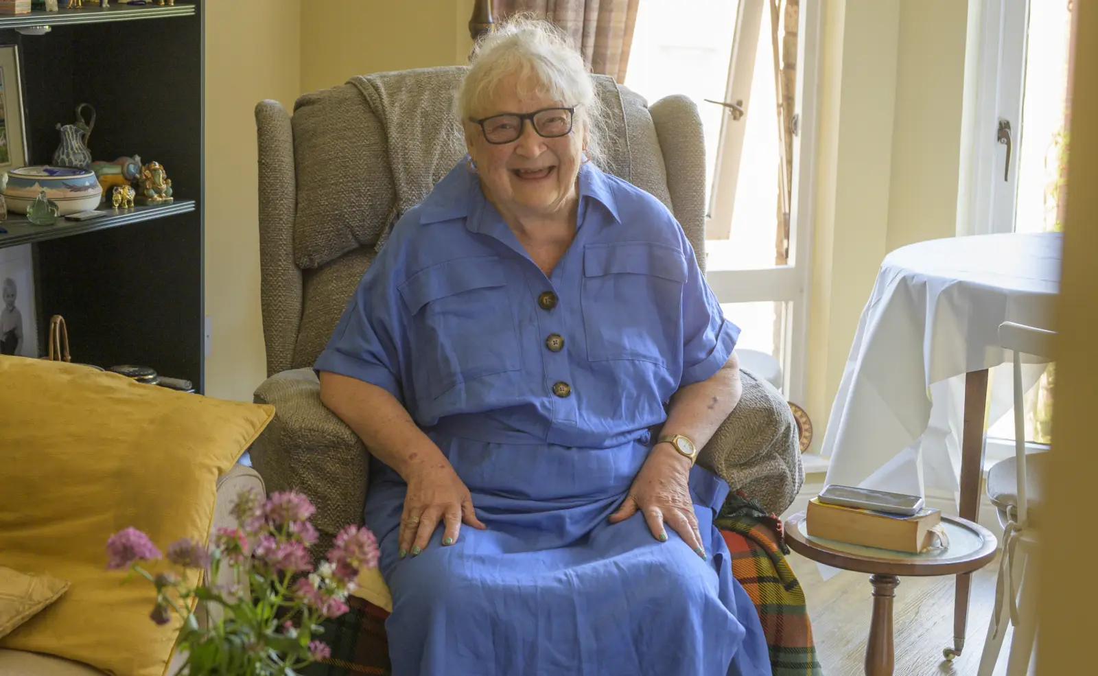 An older woman smiling in an armchair in her home