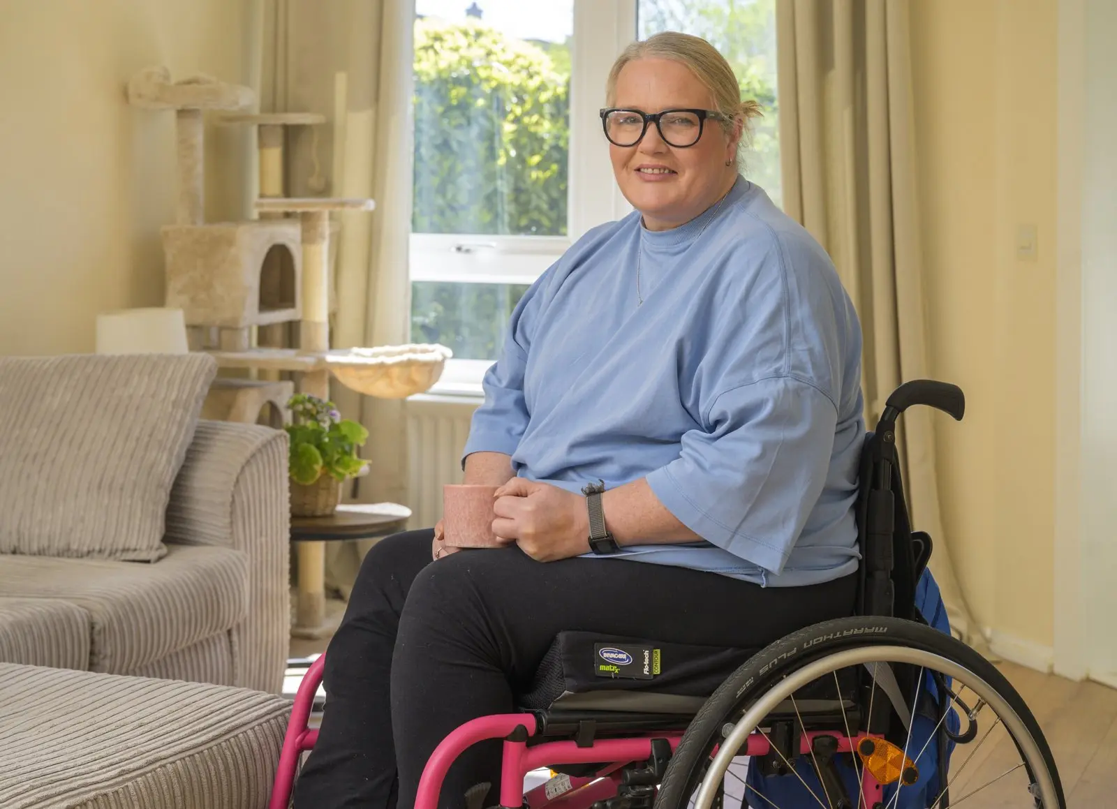 Annette at home in her wheelchair, smiling, with a mug of tea