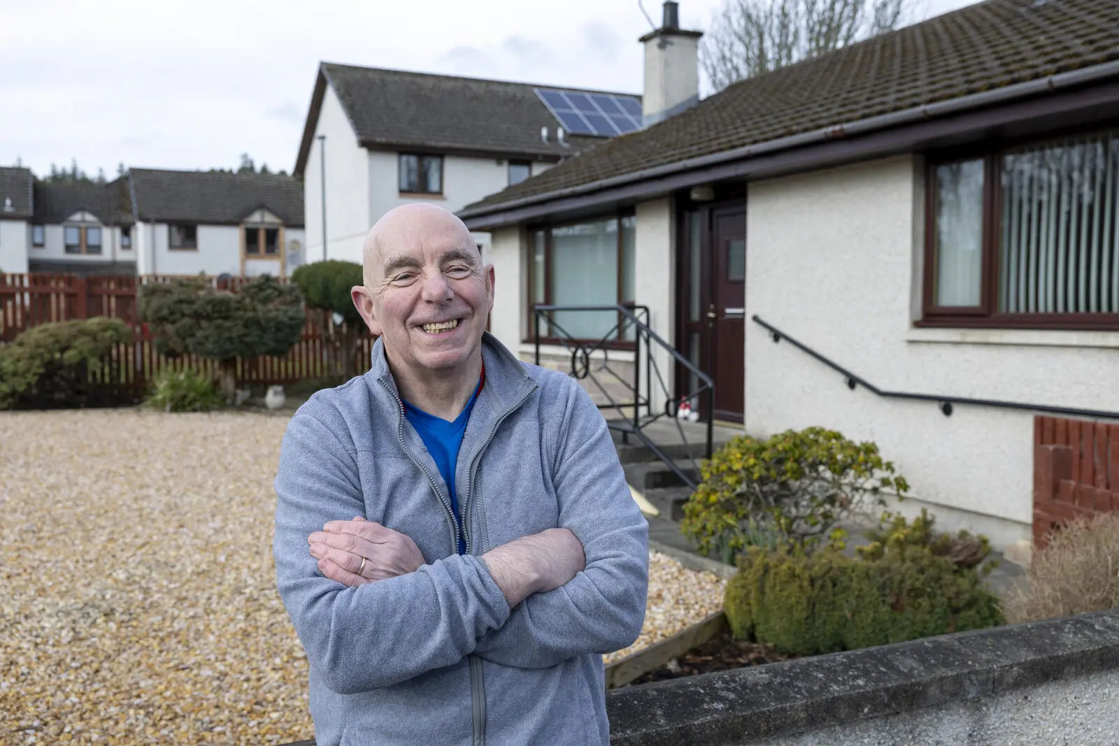 Gordon standing outside his bungalow with his arms folded, smiling