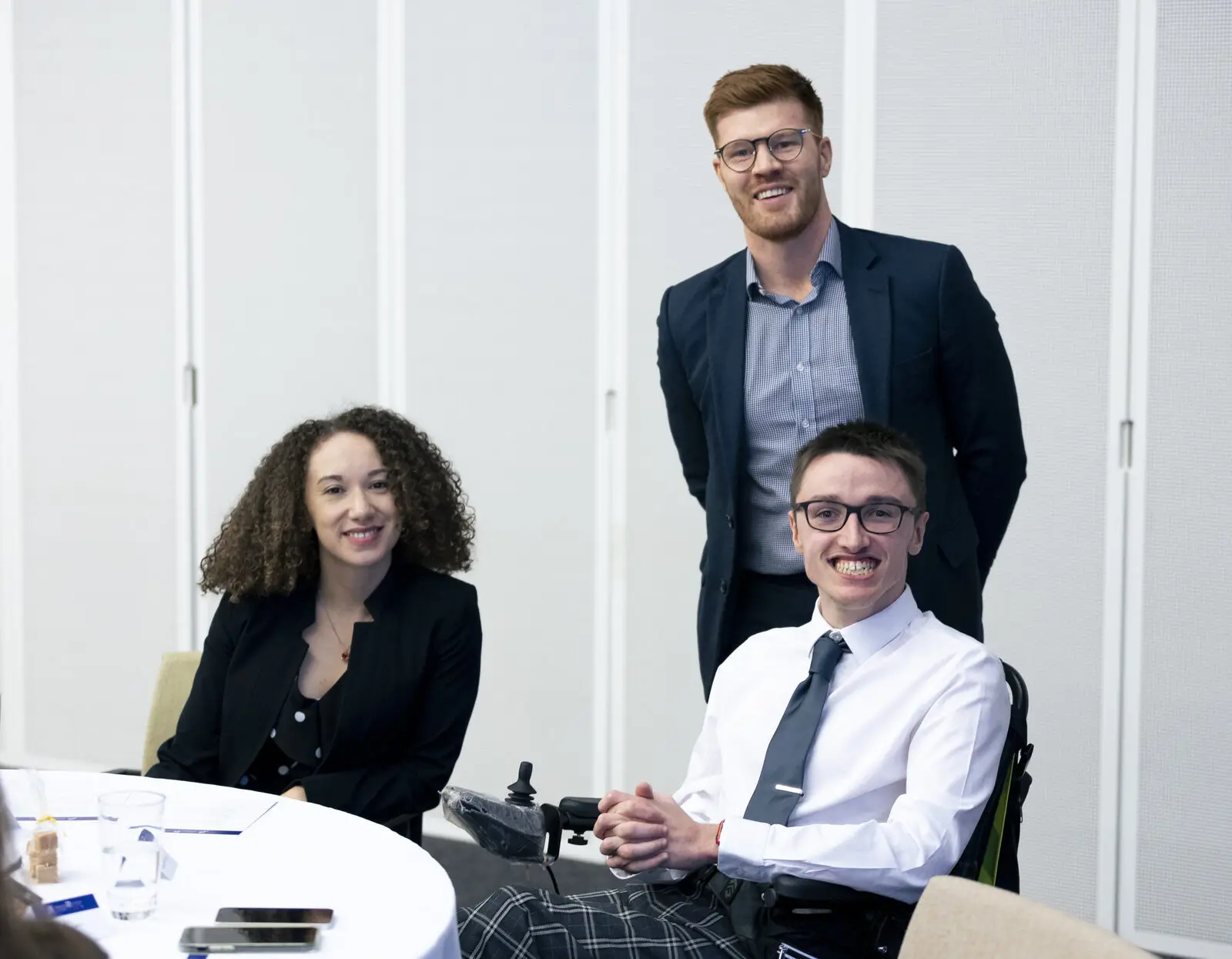 Three people smiling together at a table at a Housing Options Scotland event, one of them a wheelchair user